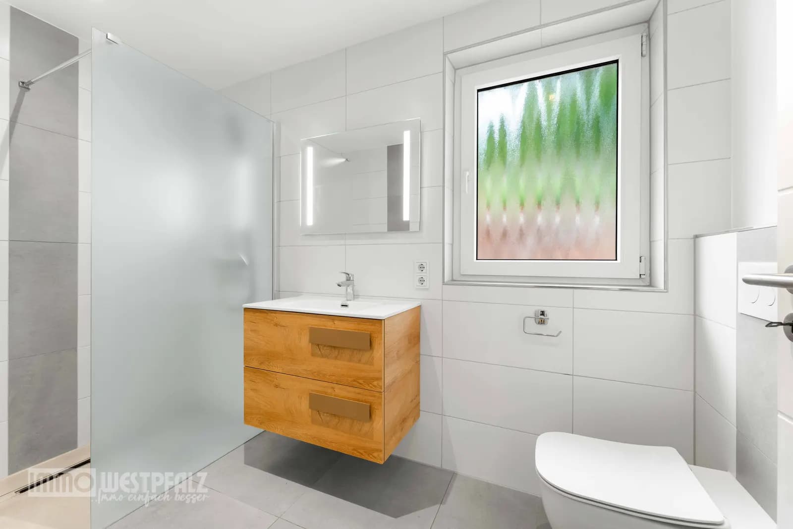 Modernes Badezimmer mit Holz-Waschtisch, bodengleicher Dusche und großformatigen Fliesen — natürliches Licht in der Immobilienaufnahme.