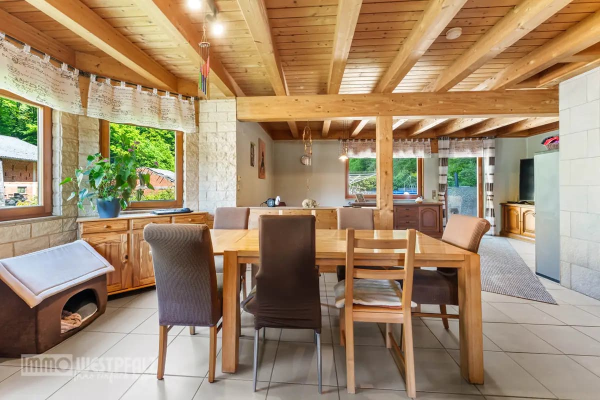 Heller Essbereich mit massiven Holzbalken, Steinwand und großem Holztisch — rustikale Innenaufnahme für die Immobilienvermarktung.