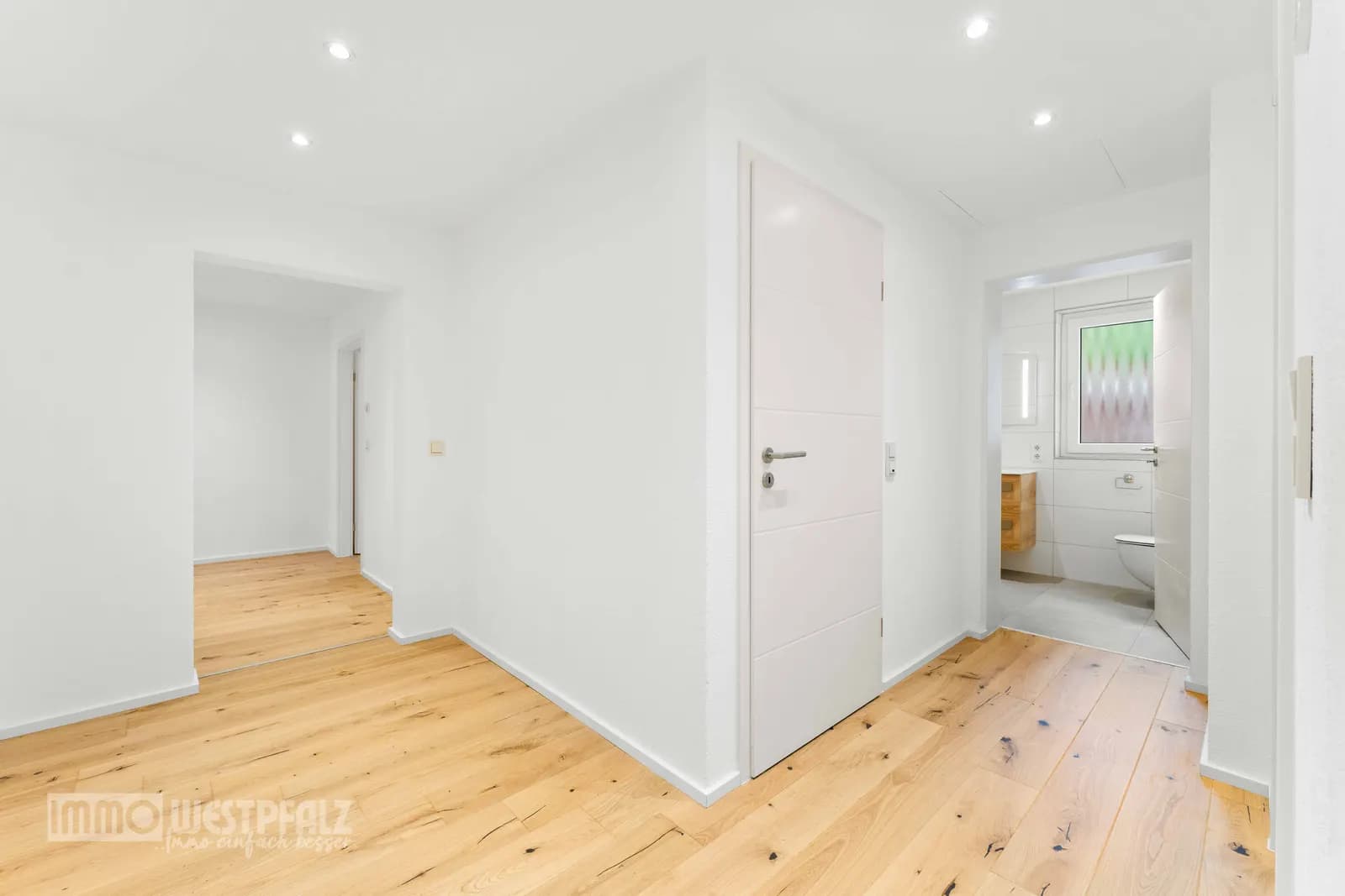 Heller Flur mit Holzfußboden und Blick in ein modernes Badezimmer — professionelle Immobilienfotografie in der Südwestpfalz.