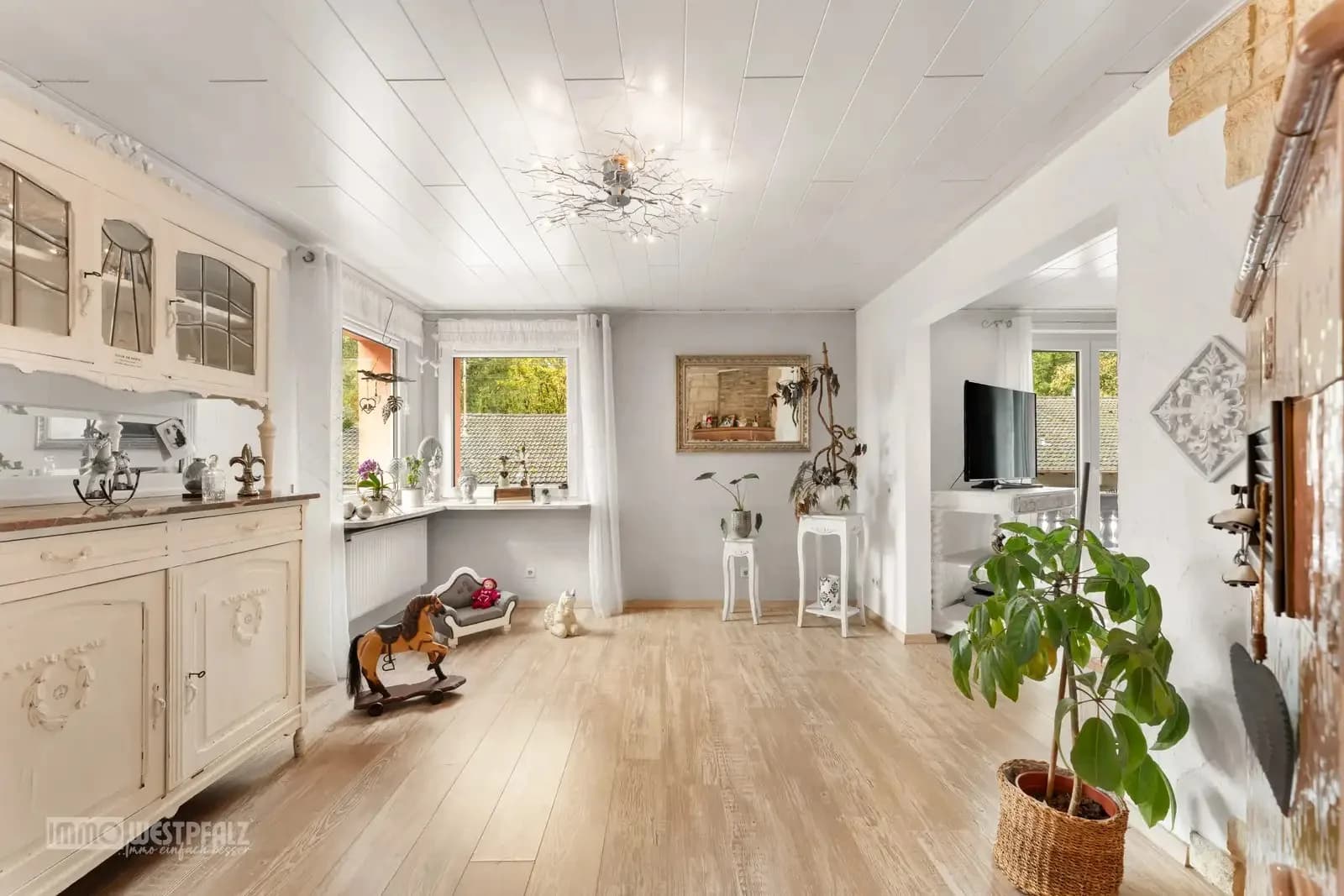 Heller Wohnbereich mit hellem Holzboden, antiker Kredenz und natürlichem Lichteinfall durch große Fenster — professionelle Immobilienfotografie.