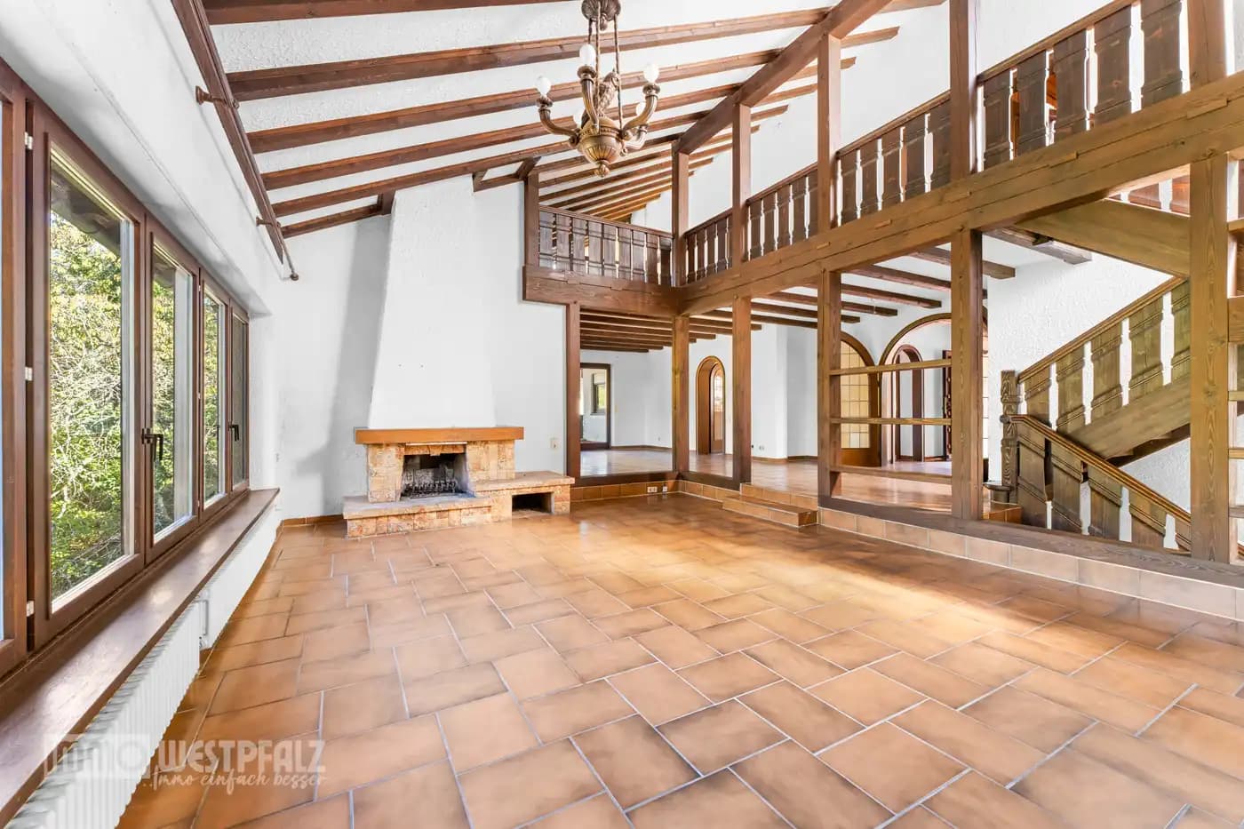 Großzügiger Wohnraum mit rustikalem Steinkamin, Terracotta-Boden und freiliegenden Holzbalken — helle Weitwinkelaufnahme für die Immobilienvermarktung.